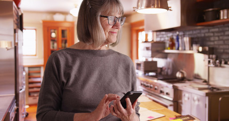 Happy senior woman sending text messages in domestic kitchen setting