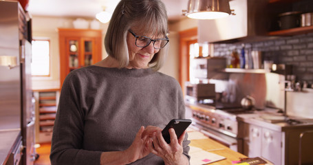Happy senior woman sending text messages in domestic kitchen setting