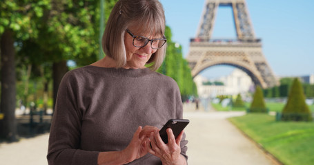 Lovely mature woman by Eiffel Tower using smart phone device to send texts