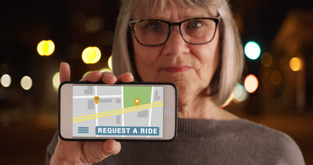 Old woman showing phone screen to camera with rideshare application open - obrazy, fototapety, plakaty