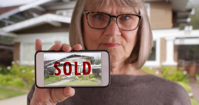 Elderly white woman holding phone with picture of home that was recently sold