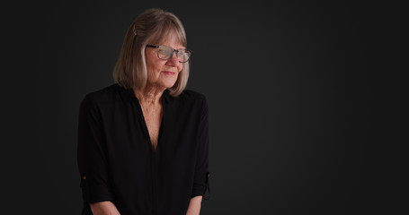 Somber senior lady thinking to herself seated alone on gray background