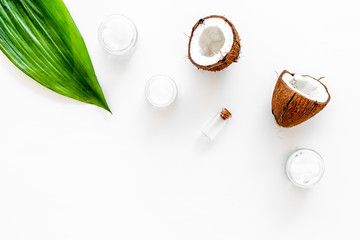 Coconut oil cosmetics for skin and hair care. Oil in small bottle, cream jar, halfs of coconut with shelf, palm leaves on white background top view copy space
