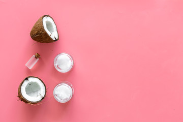 Cosmetics based on coconut oil. Oil in small bottle, cream, coconut pulp, half of coconut with shelf on pink background top view copy space