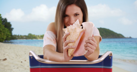 Close-up of conch shell being held by woman out of focus in background at beach
