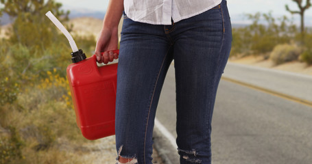 Tight shot of waist of woman with gasoline canister standing by desert road