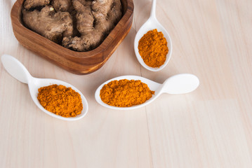 Turmeric powder and fresh turmeric on wooden background.