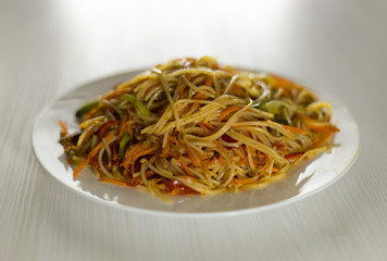 Rice noodles Funchoza with vegetables in a white plate. Traditional Korean cuisine