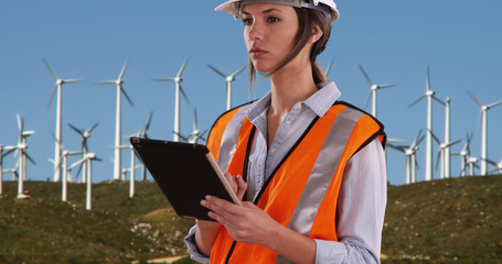 Woman in orange vest and hardhat working on tablet by wind turbines outdoors