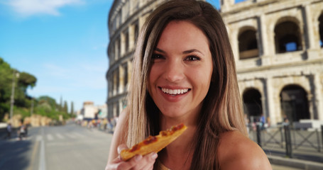 Attractive Caucasian brunette eating pizza slice happily in Rome by Coliseum