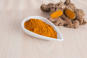 Turmeric powder and fresh turmeric on wooden background.