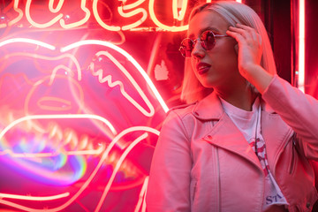 Blond girl in fashionable sunglasses and leather jacket with neon lights