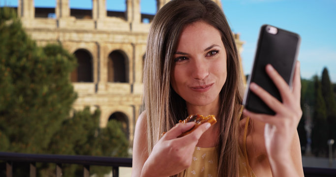 Close-up of girl taking selfie with phone while eating pizza by Coliseum in Rome
