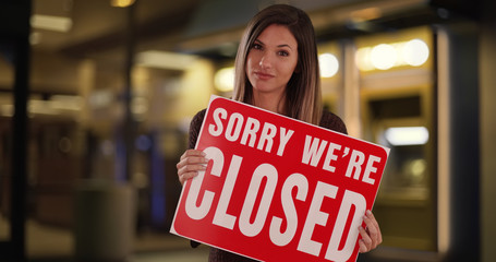 Female small business owner standing with Closed sign outside store at night