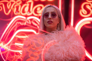 Blond girl in fashionable sunglasses and leather jacket with neon lights