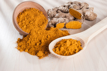 Turmeric powder and fresh turmeric on wooden background.
