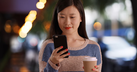 Close up of happy woman reading texts on smartphone in front of urban cafe