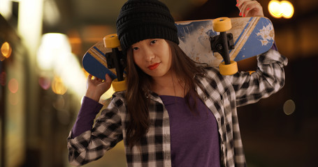 Close view of woman holding skateboard on shoulders in urban neighborhood