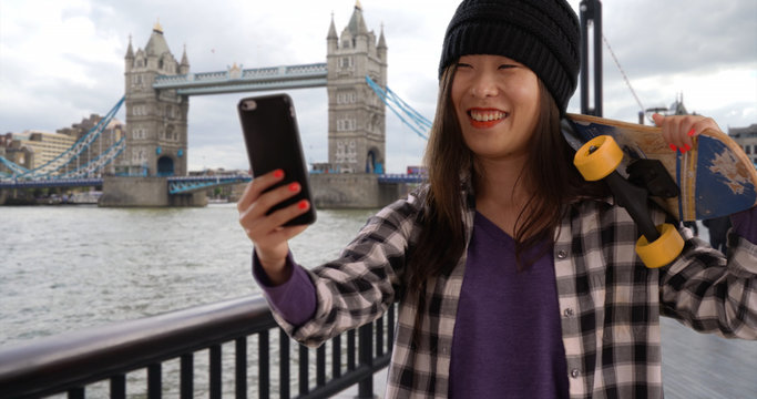 Lovely millennial skater using smart phone for selfie in London UK