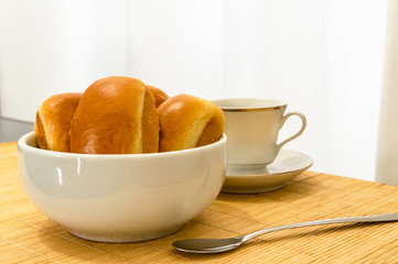 White bowl with bread, a spoon and a cup of coffee