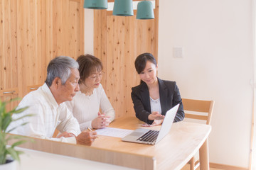 スーツの女性からパソコンで説明を受けるシニア夫婦