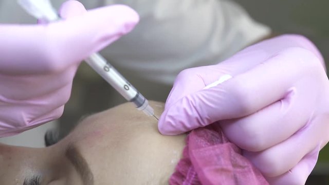 Close up handof cosmetologist making beauty injection in face. Young woman receiving botox injection for anti aging treatment. Anti wrinkle and skin care. Cosmetology concept. Plastic surgery clinic.