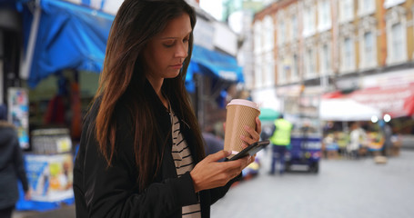Hipster girl in bomber jacket texting with cell phone in London neighborhood