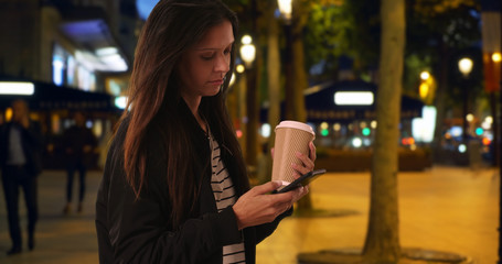 Hipster girl on the Champs-Elysees at night texting with cell phone