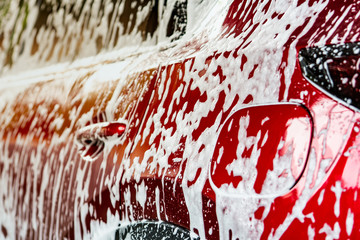 Red compact SUV car with sport and modern design washing with soap. Car covered with white foam....