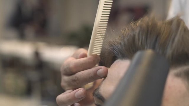 Barber using hair dryer and comb for male hairstyle in salon. Man hair drying in barber shop. Hairstylist drying hipster hair in male salon. Fashion man hairdo concept.