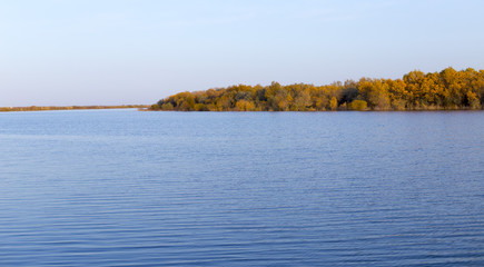 Landscape by the lake with a blue sky, yellow trees on the water with reflection