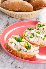 Slice of baguette with fish paste on plate and fresh rolls in background