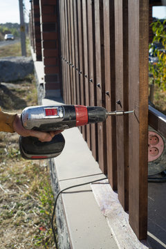 Close up of hand screewing wood plank to metal construction. Building a wooden fence with a drill and screw.