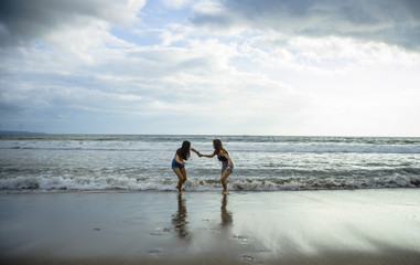  two young women friends or sisters playing together in the beach on sunset light having fun enjoying summer holidays trip in girlfriends love and friendship concept