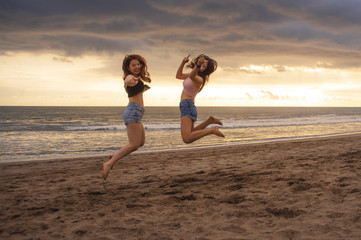 Fototapeta premium lifestyle portrait of two happy and attractive young Asian Korean women girlfriends jumping on sunset beach excited and cheerful enjoying summer holidays