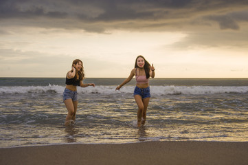 two happy and attractive young Asian Chinese women girlfriends or sisters having fun playing in the sea on sunset beach in beautiful light enjoying summer holidays