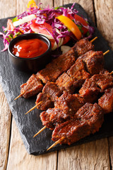 African food: spicy suya kebab on skewers with fresh vegetable salad and ketchup close-up. vertical
