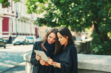 Portrait of cheerful girls in the city . Young women on the streets use modern technology . Women with tablet