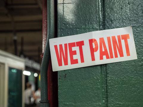 Wet paint sign hanging on green pillar in underground subway location