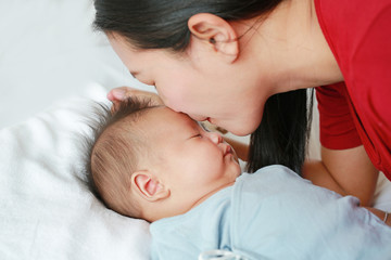 Obraz na płótnie Canvas Close up mother kissing baby boy lying on the bed.