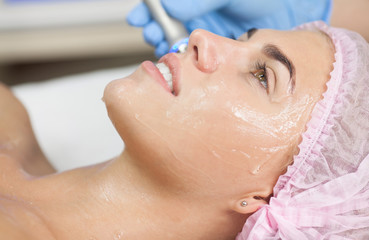Beautiful woman getting radio frequency lifting on her face. Professional beautician doing...