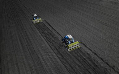 Aerial view of two blue tractors plows the earth in field on a summer day against a black earth...