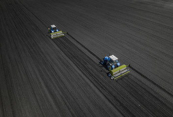 Aerial view of two blue tractors plows the earth in field on a summer day against a black earth background. Agriculture. Two tractors travel one after another along the black field
