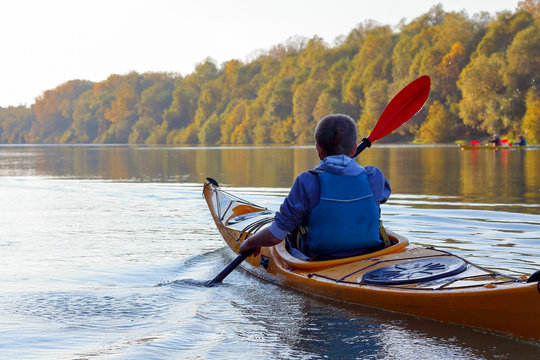 A guy in a yellow kayak rowing in the autumnal river Danube on a calm autumn day