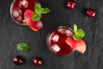 Overhead photo of two vibrant red drinks with cherries on black