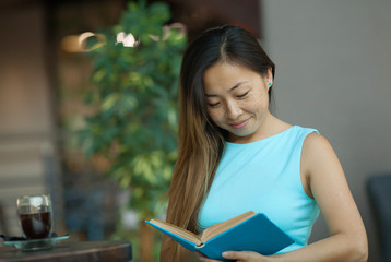 beautiful young asian woman reading a book in cafe