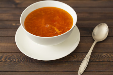 Chicken soup with vegetables and herbs in a white bowl on a wooden table