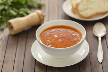 Chicken soup with vegetables and herbs in a white bowl on a wooden table