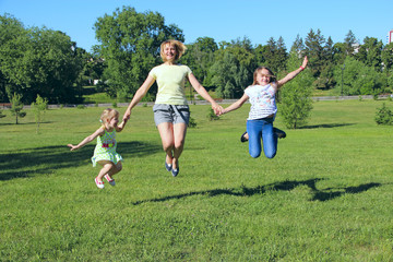 Fototapeta premium Happy mother having fun jumping with her daughters on green grass