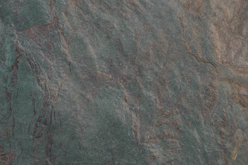 Empty dark granite rock background with green hues and impregnations of gold color. Natural stone texture